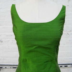 May include: A sleeveless, emerald green dress with a scoop neckline. The dress is made of a smooth, silky fabric.