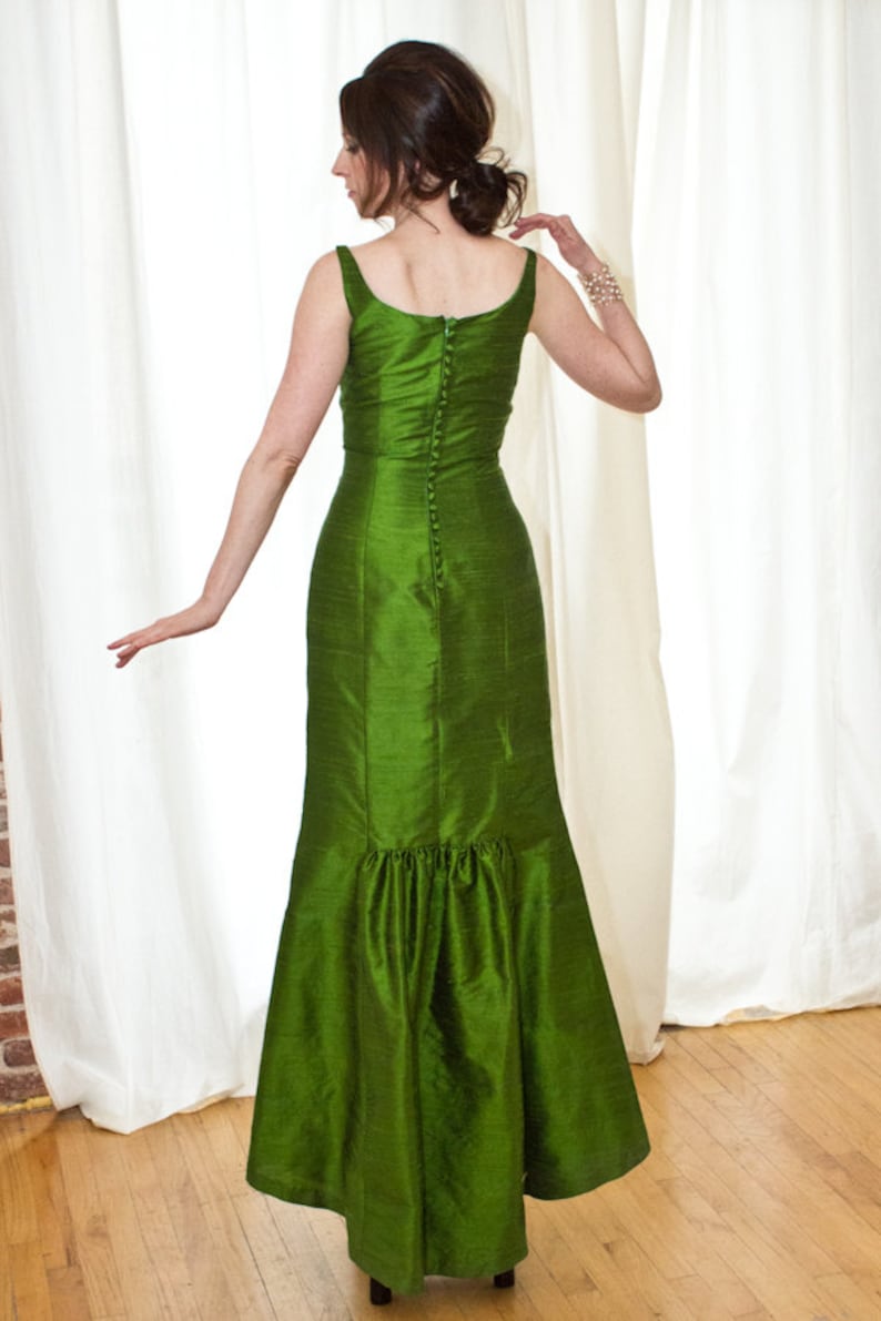 May include: A long green dress with a fitted bodice and a flowing skirt. The dress has a button closure down the back.