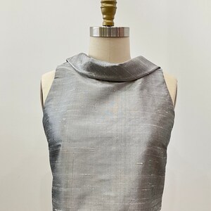 May include: A silver sleeveless top with a high, folded collar. The top is made of a textured fabric with a subtle sheen.