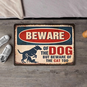 Könnte beinhalten: Rechteckiges Metallschild mit Used-Look. Auf dem Schild steht "BEWARE OF THE DOG BUT BEWARE OF THE CAT TOO" in Rot, Weiß und Blau. Eine Silhouette von Hund und Katze ist abgebildet.