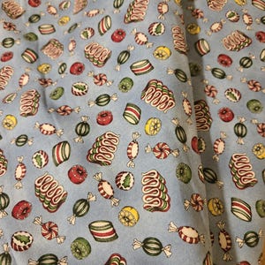 May include: Light blue fabric with a repeating pattern of colorful candies. The candies include red, green, and white striped hard candies, spiral candies, and wrapped candies. The fabric is suitable for various craft projects.
