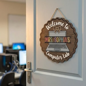 May include: A wooden sign with a scalloped edge hangs on a door. The sign reads "Welcome to MRS. SOPHIA'S Computer Lab" with a laptop graphic. The text and laptop are white, and the name is in colorful letters. A bow graphic is above the laptop.