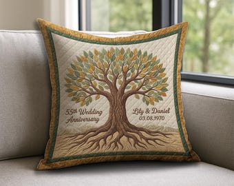 May include: Square cushion featuring a tree design with brown roots, trunk, and branches, and green and yellow leaves. The cushion has the text "55th Wedding Anniversary" and names and a date. It has a quilted pattern and a green border.