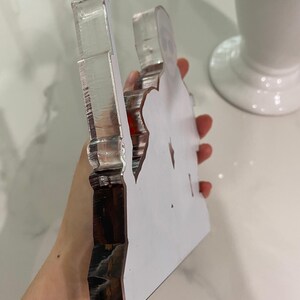 May include: A thick, clear acrylic cutout featuring a printed graphic of a person wearing sunglasses. The object has a smooth, transparent side profile with visible layered edges and a flat, white-backed surface displaying the character design.