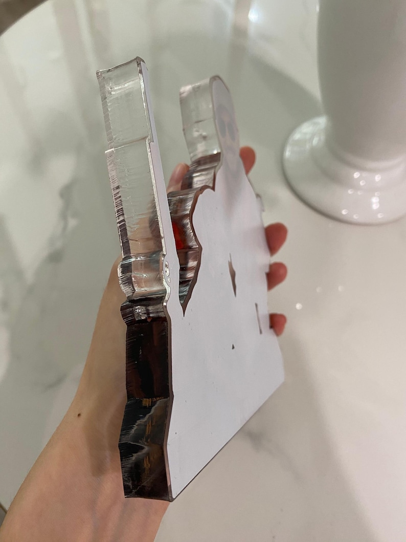 May include: A thick, clear acrylic cutout featuring a printed graphic of a person wearing sunglasses. The object has a smooth, transparent side profile with visible layered edges and a flat, white-backed surface displaying the character design.