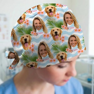 May include: A scrub cap featuring a repeating pattern of a woman's face labeled Emma and a golden retriever's face labeled Billy, interspersed with pink hibiscus flowers and green palm leaves on a light blue wavy background.