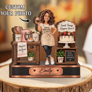 Könnte beinhalten: Ein individueller Tischaufsteller mit einer Figur in einer Schürze, die einen Cupcake hält, neben einer Kücheninsel mit Mixer, Utensilien und Mehlbehälter. Ein Schild trägt die Aufschrift Sweet Things Happen Here und eine Kupferplatte den Namen Emily.