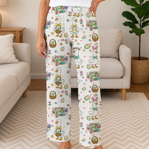 Puede incluir: Pantalones de pijama blancos con un estampado repetido de gansos de dibujos animados con cestas de Pascua, huevos y flores. El texto "Just an egg-cited goose" tambi&eacute;n est&aacute; impreso. Los pantalones son de un material suave y c&oacute;modo.