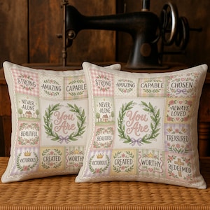May include: Two square decorative pillows with a patchwork design. Each pillow features the words "You Are" in a floral wreath, surrounded by inspirational words like "Strong," "Amazing," and "Beautiful." The pillows have a cream background.