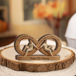May include: Wooden infinity symbol sculpture with two figures holding hands, inscribed with "My Favourite Place" and "In the world is next to you." The base reads "Brian ❤ Tommy."