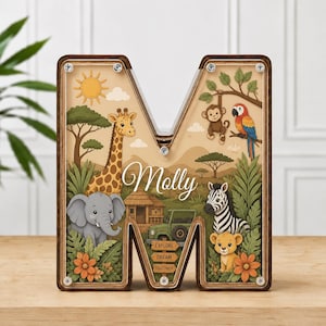 Könnte beinhalten: Eine hölzerne Spardose in Form des Buchstabens M mit einer transparenten Vorderseite. Das Innere zeigt eine Safari-Szene mit Giraffe, Elefant, Zebra, Löwe, Affe und Papagei. Der Name Molly ist in weißer Schrift gedruckt, dazu Schilder mit Explore, Dream, Discover.