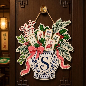 May include: A decorative wall hanging featuring a blue and white porcelain-style vase with a large letter S, filled with green pine branches, red berries, and four mahjong tiles, including one with a pink flamingo, tied with a pink ribbon.