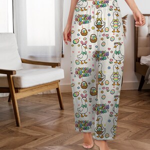 Puede incluir: Pantalones de pijama blancos con un estampado integral de gansos de dibujos animados, huevos de Pascua y cestas. El texto "Just an egg-cited goose" se repite en el dise&ntilde;o. Los gansos llevan lazos, orejas de conejo y coronas de flores.