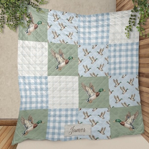 May include: Patchwork quilt with a duck design. The quilt features a square pattern with alternating squares of green, blue gingham, and duck illustrations. A label with the name "James" is visible.