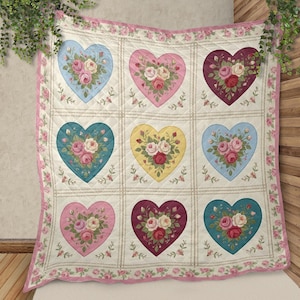 Puede incluir: Una colcha acolchada con nueve diseños en forma de corazón, cada uno lleno de un ramo de rosas. Los corazones son de varios colores pastel, incluyendo azul, rosa y amarillo, sobre un fondo crema. La colcha tiene un borde floral rosa.