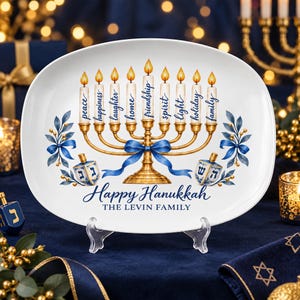 May include: An oval white ceramic platter featuring a gold menorah illustration with nine lit candles. Each candle is labeled with words like peace, happiness, and friendship. Below, the text reads Happy Hanukkah and THE LEVIN FAMILY.