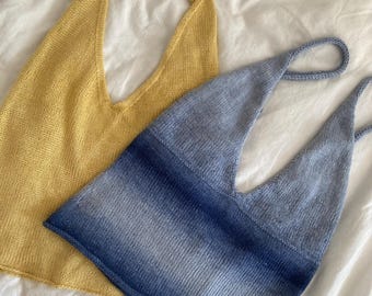 May include: Two knitted halter tops. One is a solid yellow, the other is blue with a gradient effect. Both tops have a deep V-neck and thin straps. The tops are displayed on a white surface.
