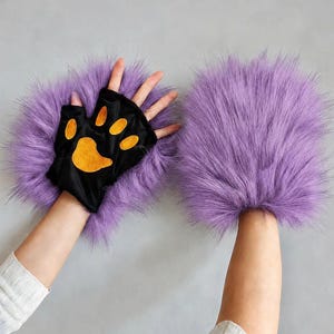 May include: A pair of fingerless gloves featuring long, vibrant purple faux fur trim. The palm side is made of black fabric and displays a prominent orange paw pad design with four smaller toe pads and one larger central pad.