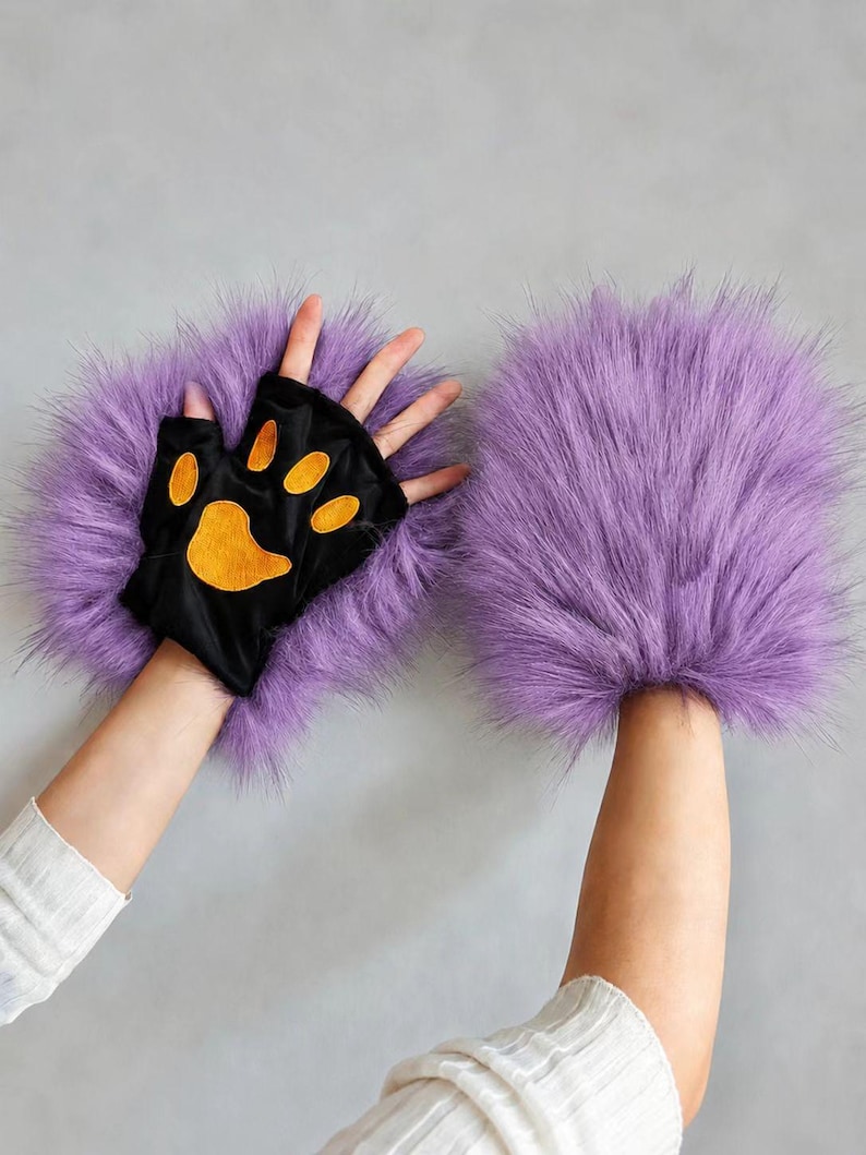 May include: A pair of fingerless gloves featuring long, vibrant purple faux fur trim. The palm side is made of black fabric and displays a prominent orange paw pad design with four smaller toe pads and one larger central pad.