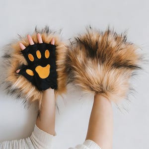 May include: Novelty gloves with a black palm and orange paw print design, surrounded by long, brown and black faux fur. The gloves are designed to resemble animal paws, perfect for costumes or fun.