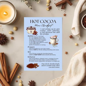 Könnte beinhalten: Eine Rezeptkarte für heiße Schokolade im Mini-Schongarer mit Zutaten und Anweisungen. Die Karte ist von Zimtstangen, Sternanis, einer brennenden Kerze und einer Schüssel mit Kakaonibs umgeben. Der Text enthält die Zutaten und Schritte.