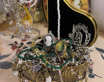 May include: A collection of vintage jewelry, including necklaces, bracelets, and earrings, displayed in a decorative gold-toned jewelry box and a glass vase. The jewelry box is ornate with floral details and a black velvet interior. A pearl necklace hangs from a black piano-shaped display.