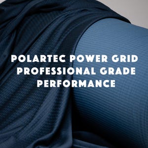 Peut inclure: Un tissu bleu marine foncé avec une texture en grille visible, drapé sur un rouleau cylindrique de matériau bleu plus clair. Le texte POLARTEC POWER GRID PROFESSIONAL GRADE PERFORMANCE est imprimé en blanc au centre de l'image.
