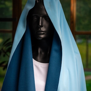 May include: A black mannequin head draped with a light blue and dark blue fabric. The light blue fabric is smooth, while the dark blue fabric has a textured pattern. The mannequin is wearing a white t-shirt.