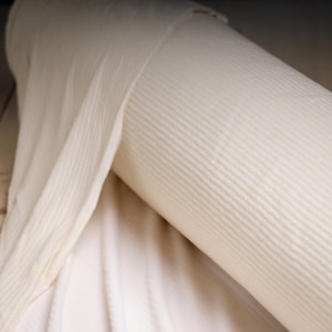 May include: A roll of off-white, ribbed fabric. The fabric is tightly rolled, revealing the texture of the material. The fabric appears to be a medium weight, suitable for various sewing projects. The color is a soft, creamy white.