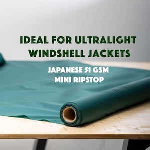 Puede incluir: Un rollo de tela color verde azulado con textura lisa. El texto en la imagen dice: IDEAL FOR ULTRALIGHT WINDSHELL JACKETS, JAPANESE 51 GSM MINI RIPSTOP. La tela está desenrollada sobre una superficie plana, mostrando un color verde oscuro.