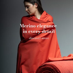 Op de afbeelding: Een persoon gehuld in een levendige rode merinowol stof. Een rol van dezelfde stof ligt op een houten oppervlak. De afbeelding bevat de tekst "Merino elegance in every detail" en "discover more".