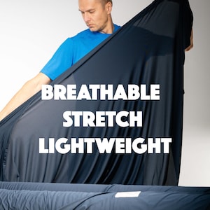 Pode incluir: Uma pessoa segura um grande pedaço de tecido azul marinho. O tecido tem a inscrição "BREATHABLE STRETCH LIGHTWEIGHT" em branco. Tecido enrolado é visível em primeiro plano. A pessoa está vestindo uma camiseta azul.