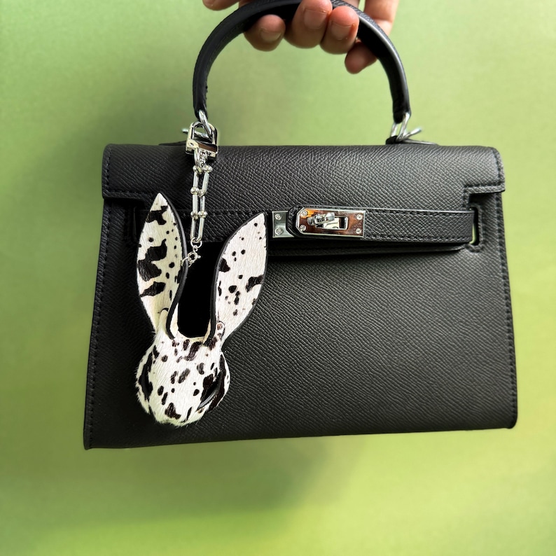 Handmade bunny leather bag charm made from horsehair and lambskin, shown hanging on a black handbag. Luxury purse charm and statement handbag charms featuring hair-on leather texture, designed as a unique bag accessory.