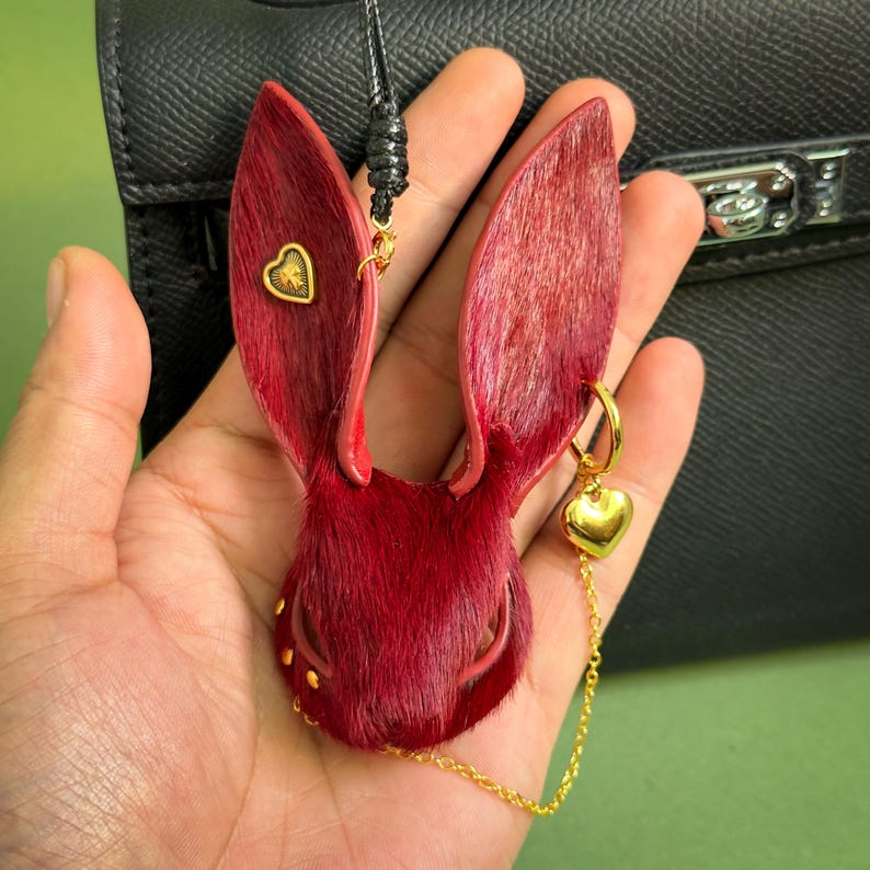 Close-up of a handmade Burgundy Gothic bunny leather bag charm shown in hand, featuring genuine horsehair texture, French lambskin backing, gold heart accents, and a delicate chain. Luxury Dark Romance purse charm designed for handbags and designer accessories.