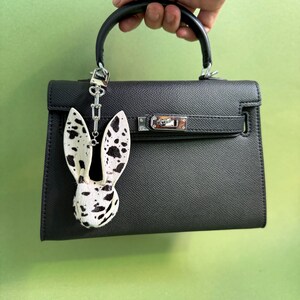 Handmade bunny leather bag charm crafted from hair-on horsehair and lambskin, displayed on a structured black handbag. Luxury purse charm and statement handbag charms with distinctive spotted hair texture, designed as a premium bag accessory.