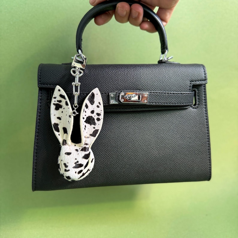 Handmade bunny leather bag charm crafted from hair-on horsehair and lambskin, displayed on a structured black handbag. Luxury purse charm and statement handbag charms with distinctive spotted hair texture, designed as a premium bag accessory.