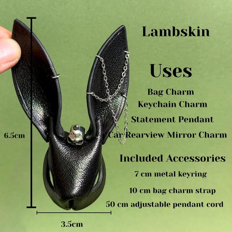 Op de afbeelding: Zwarte leren konijnenoorketting met een schedelaccent, 6,5 cm hoog en 3,5 cm breed. Inclusief een 7 cm metalen sleutelhanger, een 10 cm tasriem en een 50 cm verstelbaar pendelkoord. De tekst zegt "Lambskin" en "Uses".