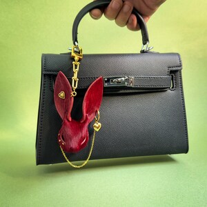 Handmade Burgundy Gothic bunny leather bag charm displayed on a black handbag, featuring genuine horsehair texture, gold heart accents, and a luxury chain detail. Dark Romance purse charm shown with long gold clip, ideal for designer bags, totes, and everyday handbags.