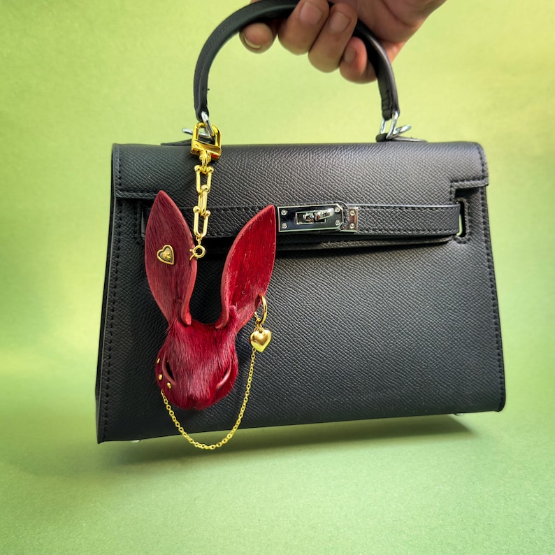 Handmade Burgundy Gothic bunny leather bag charm displayed on a black handbag, featuring genuine horsehair texture, gold heart accents, and a luxury chain detail. Dark Romance purse charm shown with long gold clip, ideal for designer bags, totes, and everyday handbags.