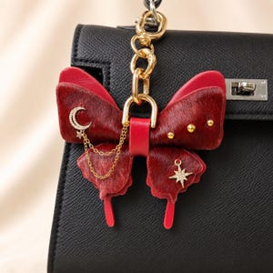 This Burgundy Gothic Vintage Leather Butterfly Bag Charm is a handmade purse charm and handbag charm, crafted from horsehair and lambskin, with gold chain, moon, and star details, also works as a keychain or car mirror pendant.