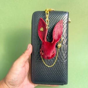 Burgundy Gothic bunny leather bag charm displayed on a black snakeskin wallet, featuring handmade horsehair leather, lambskin backing, gold heart accents, and a delicate chain. Luxury Dark Romance purse charm suitable for handbags, wallets, and designer accessories.