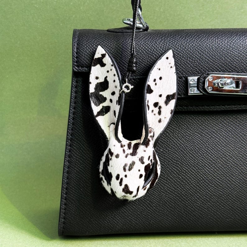 Bunny leather bag charm hanging on a black handbag, handmade horsehair and lambskin purse charm with black and white patterned hair-on leather texture. Statement handbag charm designed as bold handbag charms accessory for luxury bags and everyday purses.