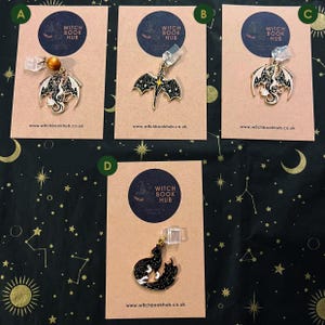 May include: Four fantasy-themed charms displayed on cards. Each card has the text "WITCH BOOK HUB" and a website address. The charms feature dragon and wolf designs in black and silver, suitable for fantasy enthusiasts.