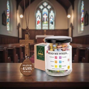 May include: A wooden cross pendant with the text "I AM WITH YOU ALWAYS" and a jar labelled "READ ME WHEN..." filled with colourful Bible verses. A small box with the text "BIBLE VERSES FOR DAD" is also present. The items are on a wooden surface.