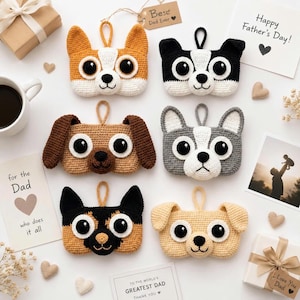 May include: Six handmade crochet dog face ornaments in various colours, including tan, black, and grey. Each ornament features large, expressive eyes and a loop for hanging. Father's Day cards and gifts are also present.
