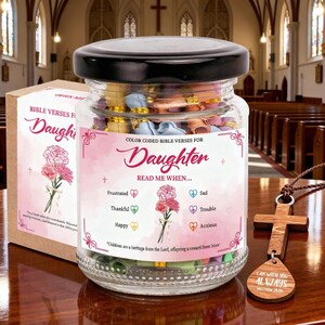 May include: A glass jar filled with colorful rolled-up papers, labeled "Color Coded Bible Verses for Daughter." The jar has a black lid and is accompanied by a wooden cross pendant with a leather cord. The text on the jar reads "Read Me When..." with various emotions.