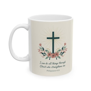 Op de afbeelding: Witte keramische mok met een donkergroen kruis en een bloemenkrans. De mok heeft de tekst "Ik vermag alle dingen door Christus, Die mij kracht geeft" uit Filippenzen 4:13.