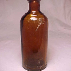 May include: A dark brown glass bottle with a rounded bottom and a narrow neck. The bottle has a slightly textured surface and appears to be old.