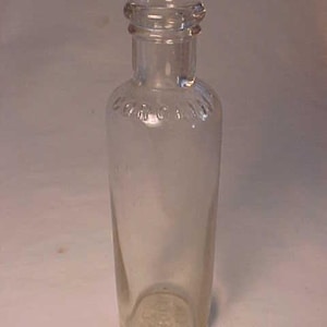 May include: A clear glass bottle with a rounded bottom and a slightly flared top. The bottle has a textured surface and is empty.