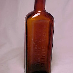 May include: An amber glass bottle with a glass stopper. The bottle is labeled "CAPUDINE" and "FOR ALL HEADACHES" with the text "SMITH, KLINE & FRENCH CO. PHILA. PA."